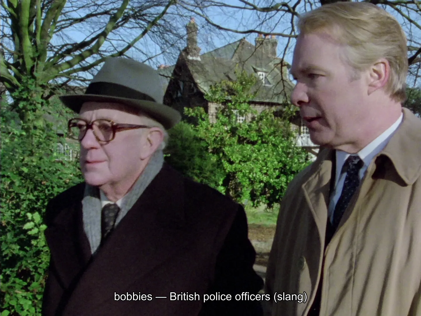 George Smiley out walking with a colleague in Tinker, Tailor, Soldier, Spy (1979), with an Explainer subtitle along the bottom reading "bobbies — British police officers (slang)"
