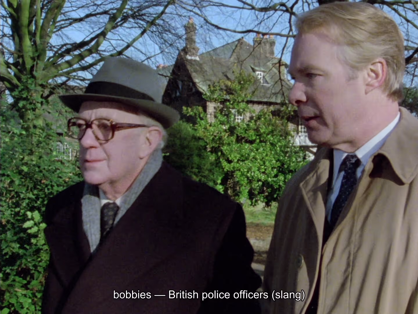 George Smiley out walking with a colleague in Tinker, Tailor, Soldier, Spy (1979), with an Explainer subtitle along the bottom reading “bobbies — British police officers (slang)”